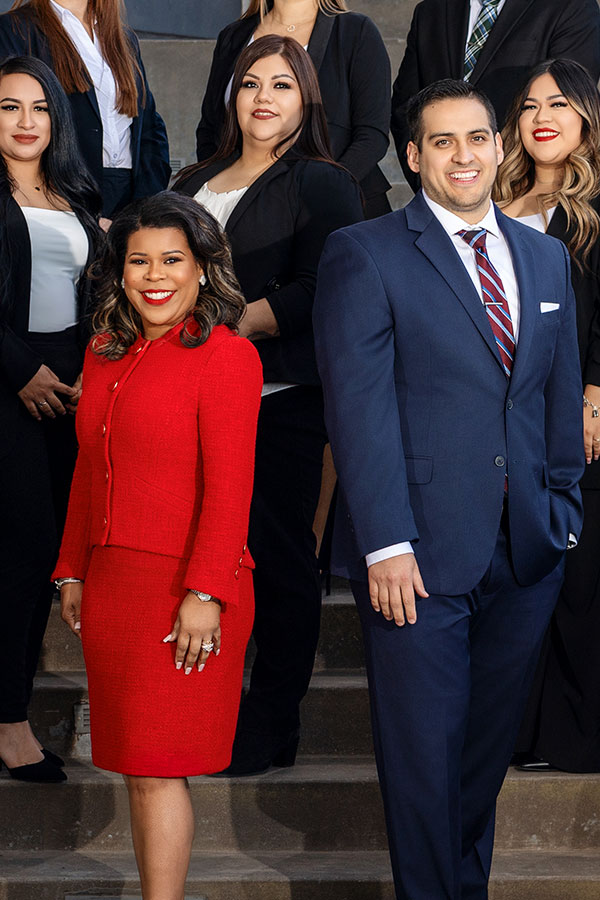 A professional group portrait of the Erika N. Salter, PC legal team. Erika Salter, wearing a bright red suit, stands in the foreground alongside a male colleague in a navy suit, with several other team members in professional attire standing behind them on outdoor steps